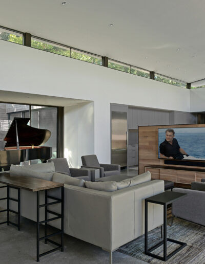 Contemporary living room with a grand piano and a large television screen, featuring minimalist design and ample natural lighting.